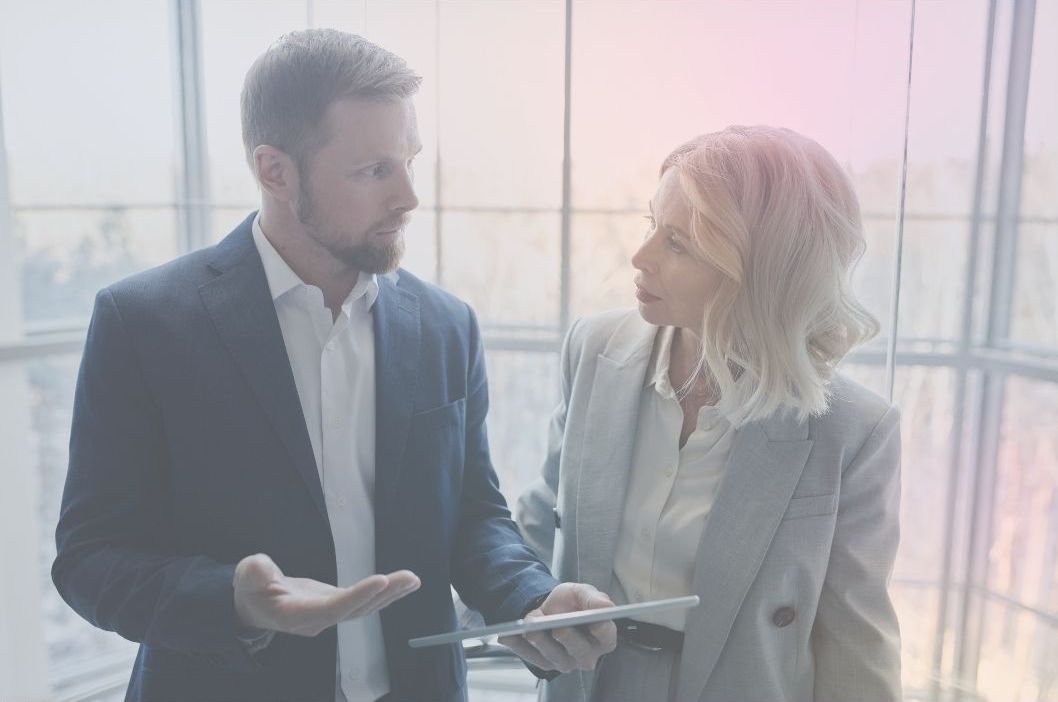 A man and a woman in suits discuss an incident while holding a tablet